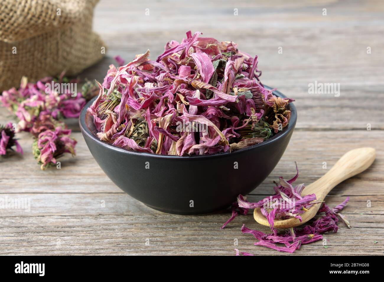 Fiori sani di echinacea in ciotola di ceramica nera e sacco di confiori secchi sullo sfondo. Medicina di erbe. Foto Stock