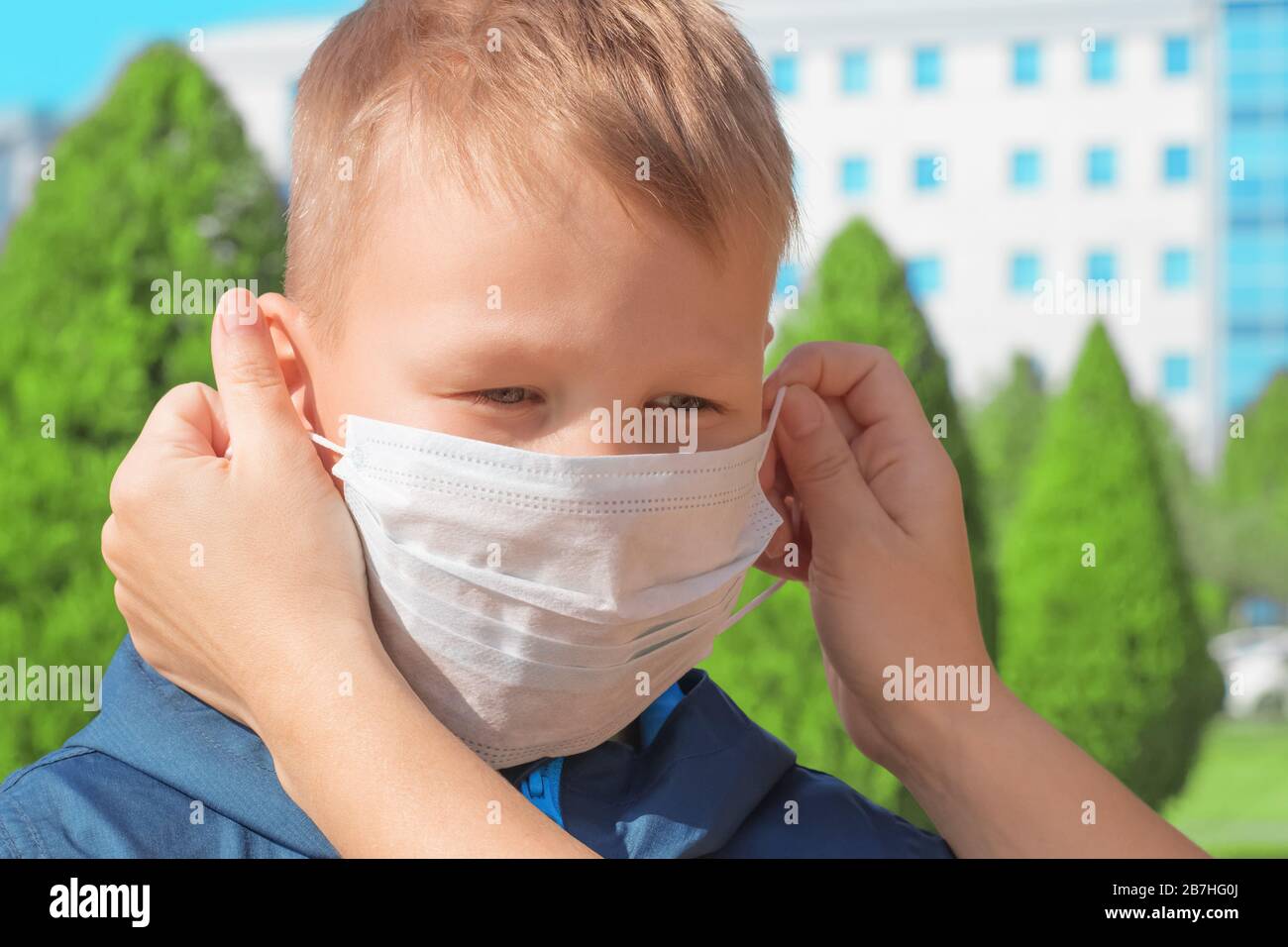 La ragazza mette su un viso del ragazzo una maschera medica protettiva per la prevenzione delle malattie virali Foto Stock