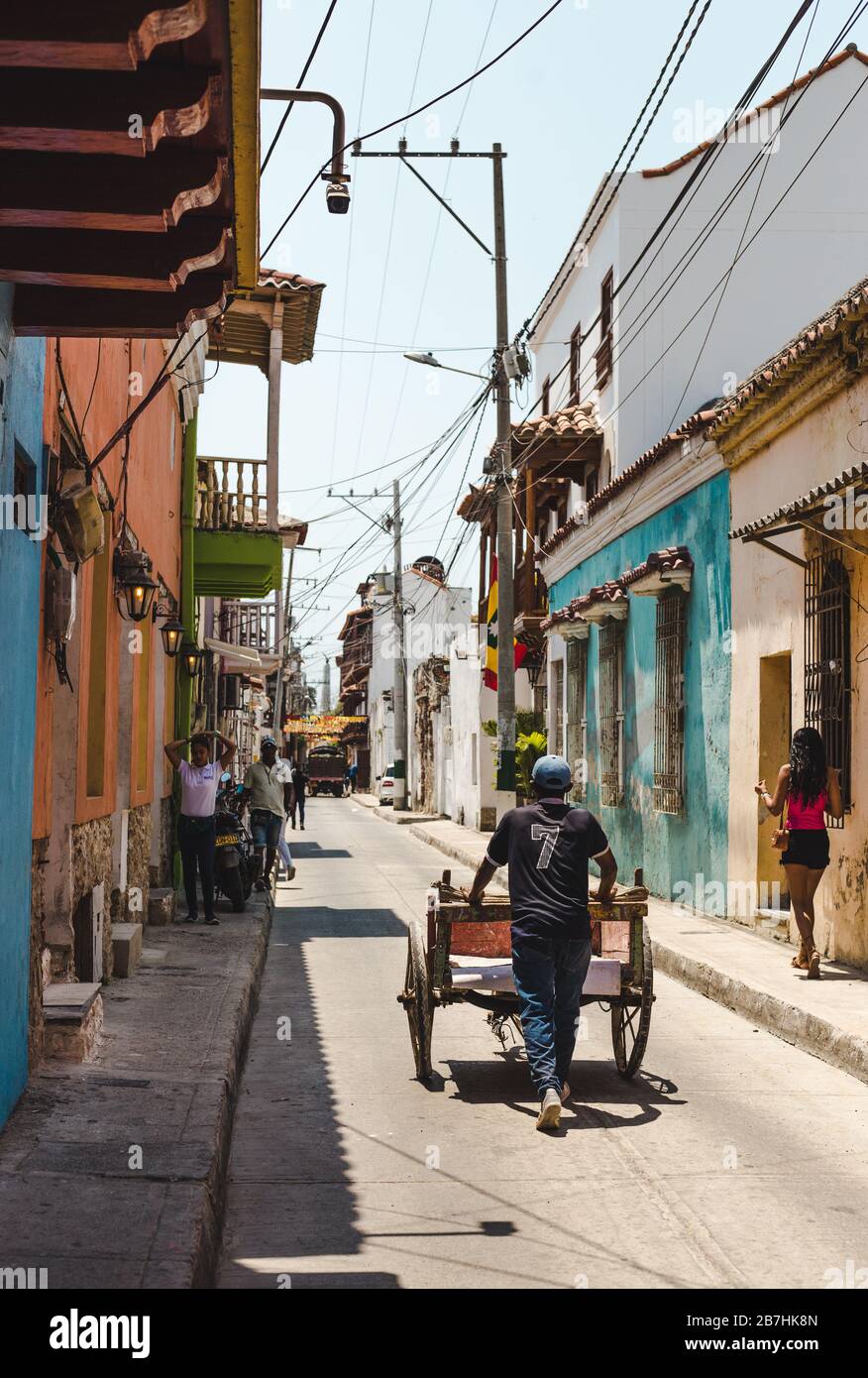Uomo di lavoro che spinge il carrello di legno dei prodotti lungo una strada stretta colorata nel centro di Getsemani, Cartagena Foto Stock