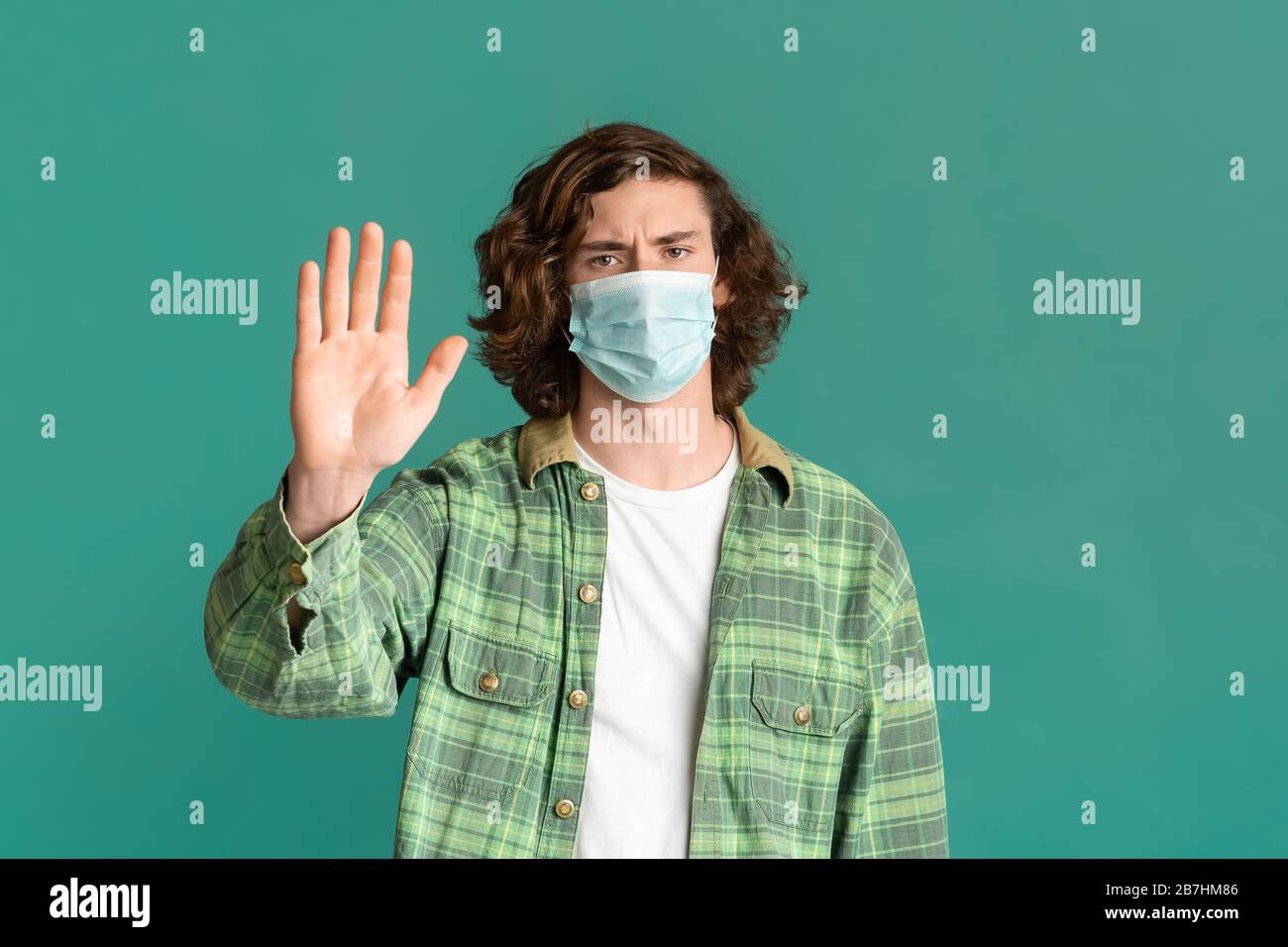Epidemia. Giovane ragazzo che indossa la maschera e mostra IL gesto STOP su sfondo turchese Foto Stock
