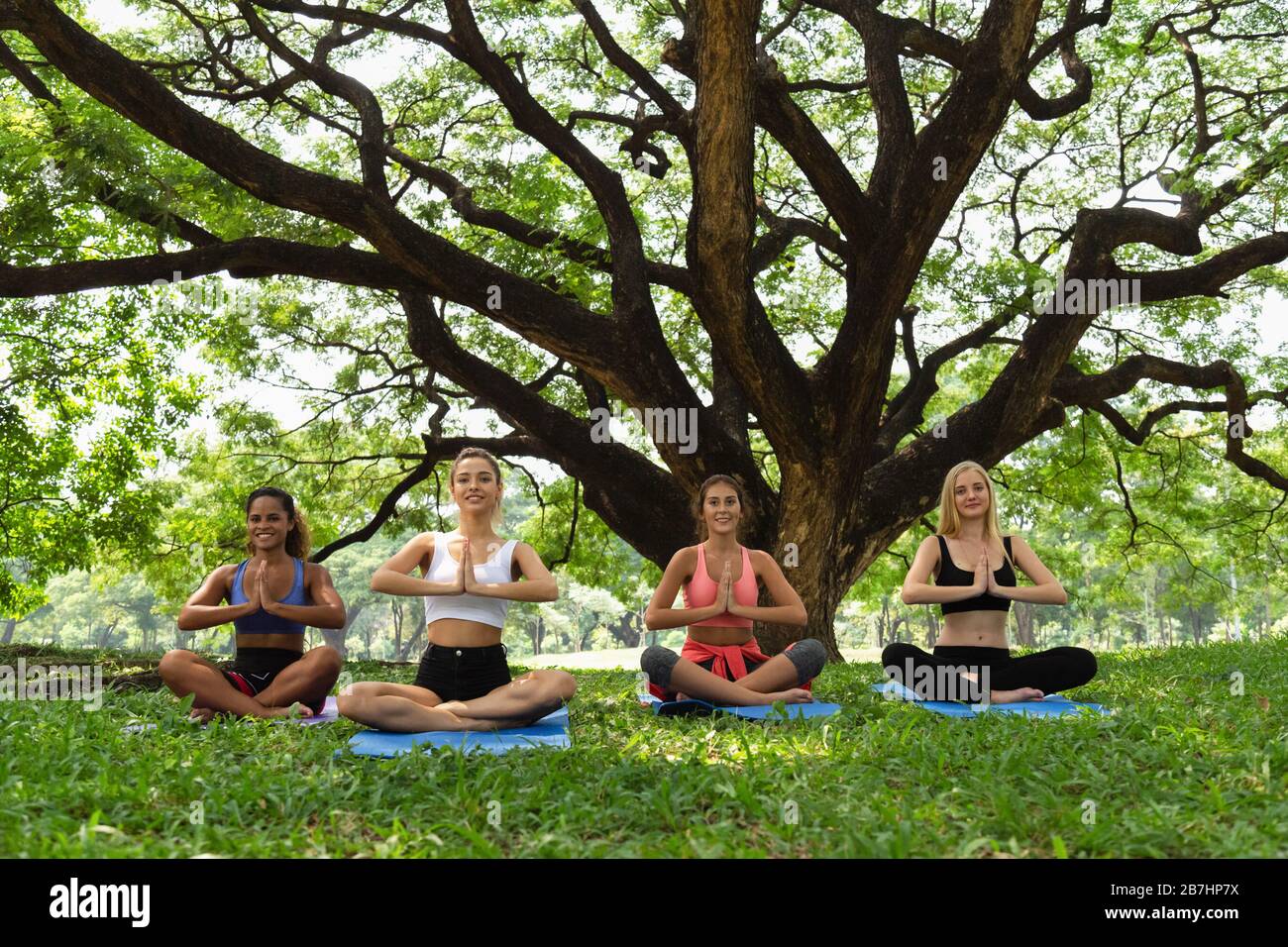 buon sano quattro donne adolescenti allenarsi e praticare il fuoco ceppo yoga posa nel parco al mattino. sano, sport e stile di vita concetto. Foto Stock