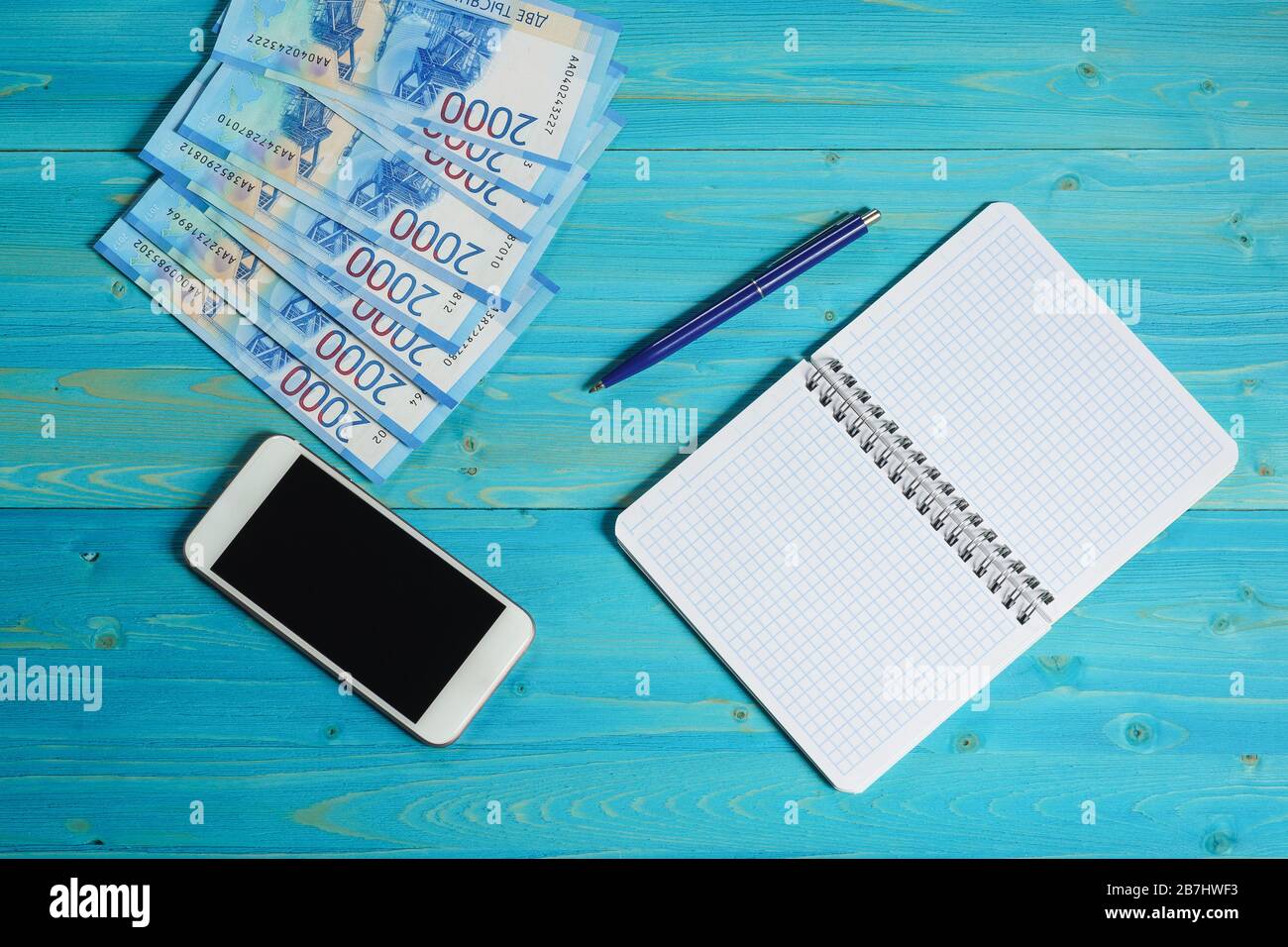 Un notebook vuoto per banconote, banconote russe e uno smartphone su un tavolo di legno. Pianificazione della spesa familiare Foto Stock