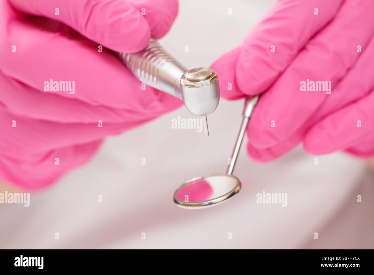 Mani del dentista ravvicinate in guanti di lattice rosa con specchio per la  bocca e manipolo odontoiatrico ad alta velocità su sfondo sfocato. Concetto  di strumenti medici. Poco profondo Foto stock -