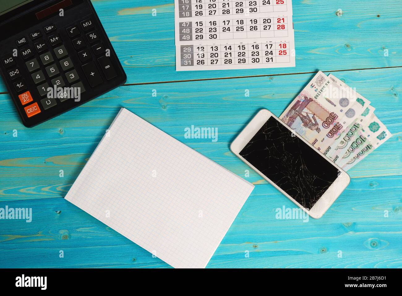 Calendario, notebook pulito, smartphone rotto e denaro russo sul tavolo blu. Le spese impreviste hanno interrotto i piani Foto Stock