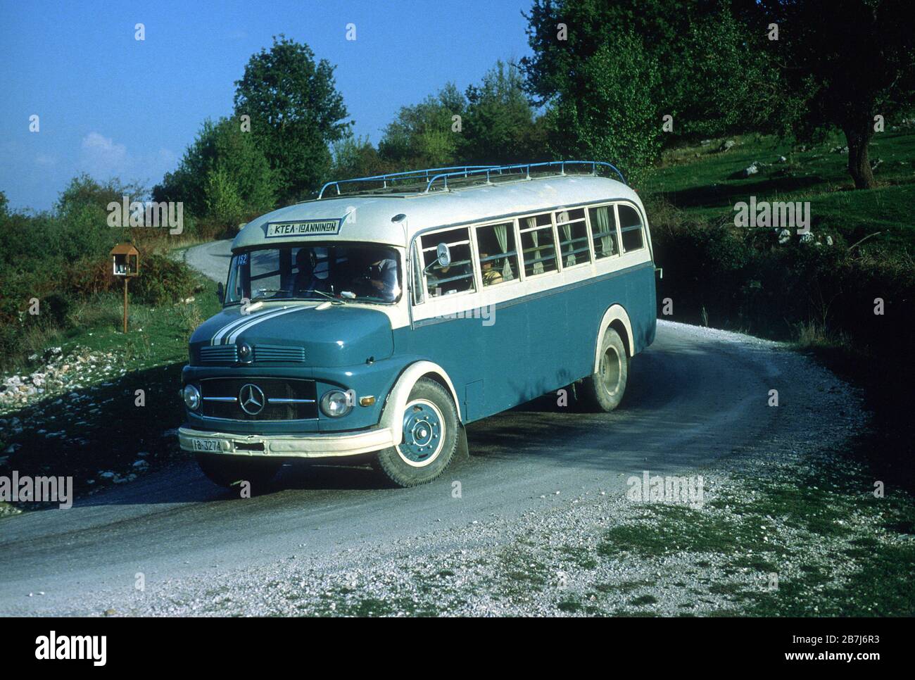 L'autobus per Ioannina. Uno dei vecchi, robusti, blu e bianchi, Mercedes autobus che un tempo era comune sulle strade della Grecia. Vicino all'antica Dodoni. Passa davanti a un santuario a lato della strada sulla curva. Questi sono comunemente eretti al punto che qualcuno è stato ucciso in un incidente stradale. Foto Stock