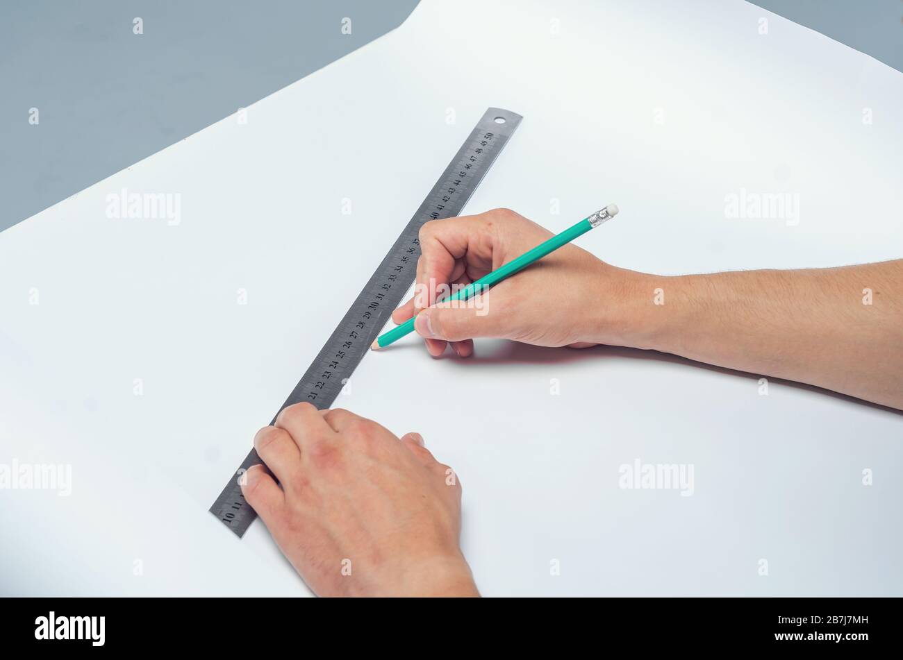 La mano maschile disegna la matita sotto un righello su un foglio bianco di carta Foto Stock