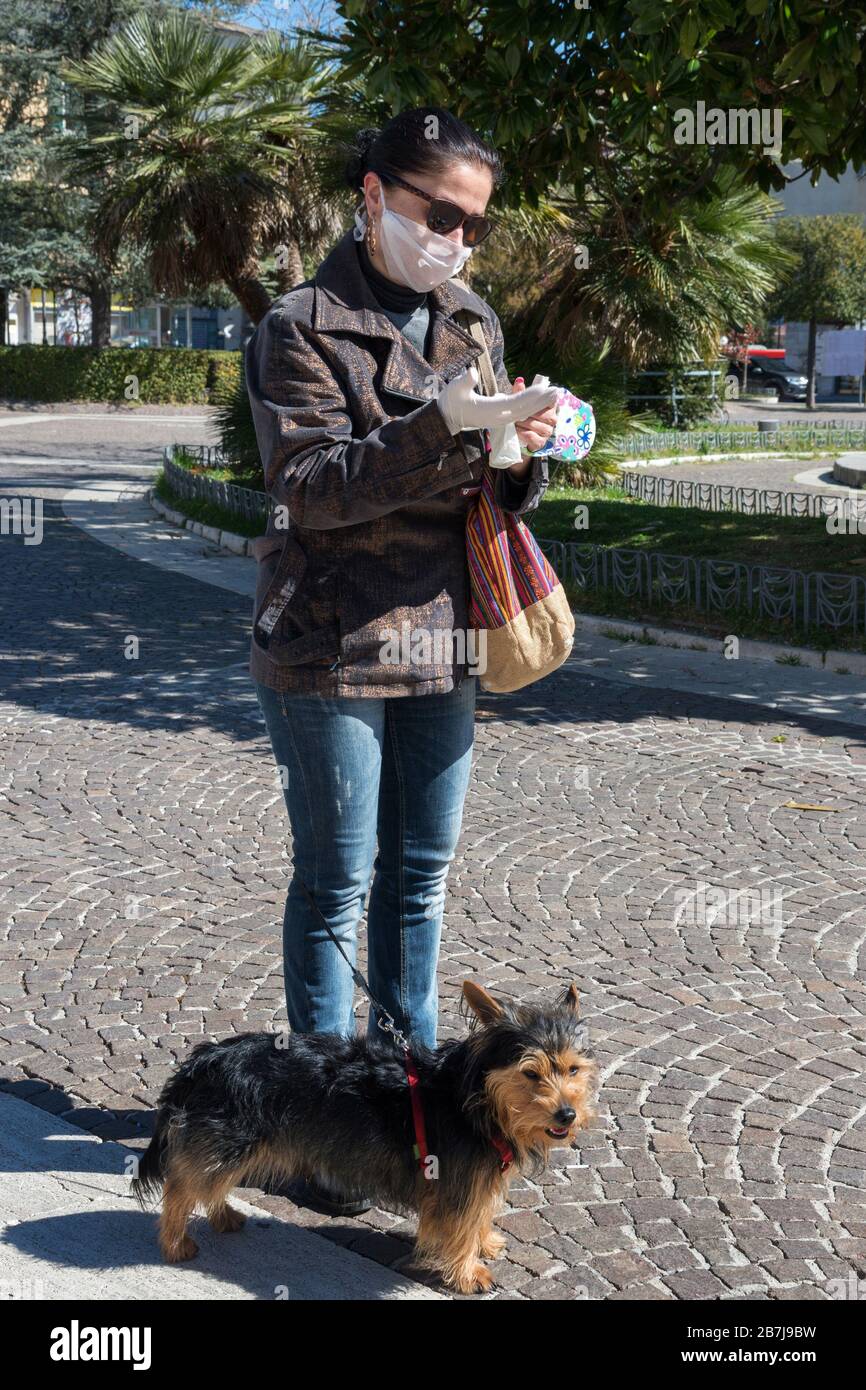 Campobasso,Regione Molise,Italia:una donna con maschera protettiva che cammina con il suo cane mette i guanti per la sicurezza durante i giorni del coronavirus a Campobasso Foto Stock