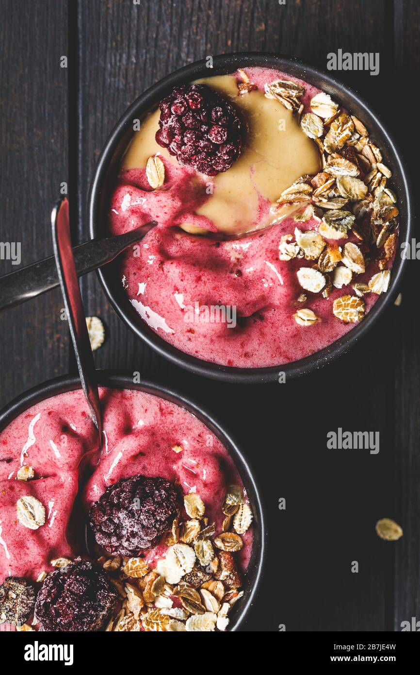 Ciotola di frullato di frutti di bosco con tahini e muesli, sfondo scuro. Gelato alla bacca fatto in casa con burro di arachide e granola. Foto Stock