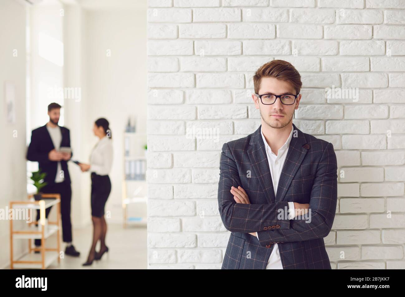 Uomo d'affari serio in abbigliamento casual in piedi in un ufficio bianco su una parete bianca. Foto Stock