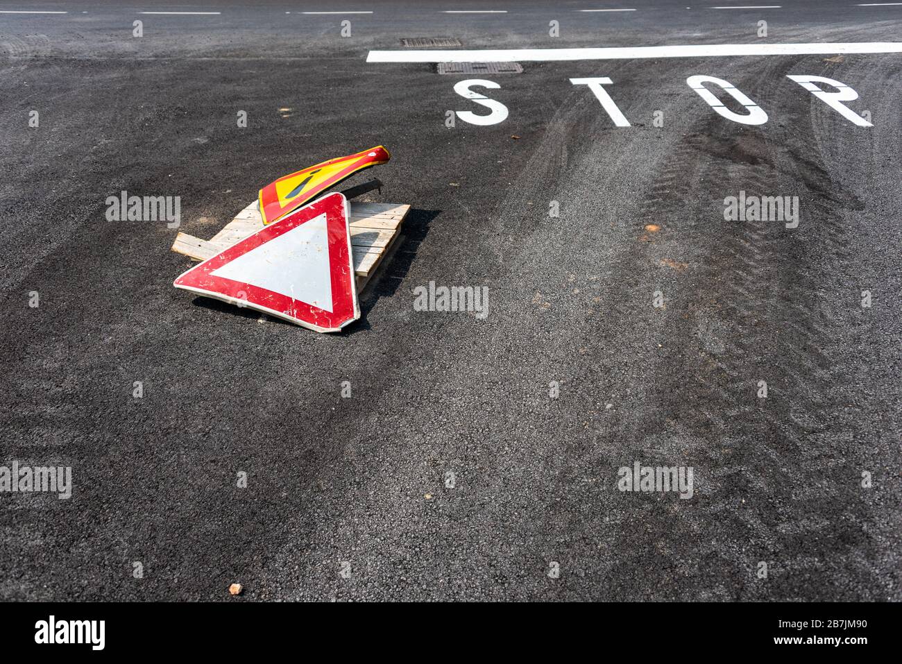 Punto esclamativo del segnale di avvertimento nel triangolo giallo e prestare attenzione al segnale a destra sulla strada asfaltata con il segnale di stop bianco Foto Stock