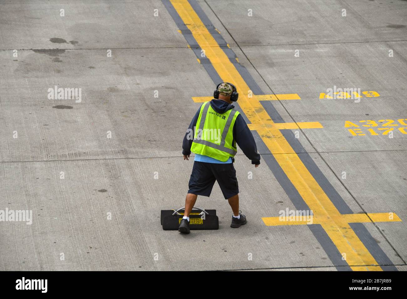 AEROPORTO DI SEATTLE TACOMA, WA, USA - GIUGNO 2018: Lavoratore dell'aeroporto con gilet ad alta visibilità e protezioni acustiche all'aeroporto di Seattle Tacoma, e una serie di cunei per ruote Foto Stock