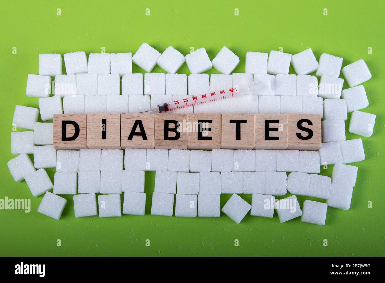 diabete di parola in blocchi di legno circondato da cubetti di zucchero su sfondo verde, siringa Foto Stock