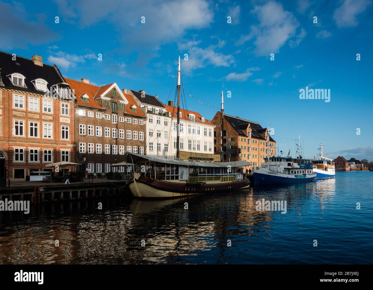 Famoso porto vecchio con barche e colorati vecchi edifici a Copenhagen, Danimarca. Giornata di sole con bei riflessi in acqua. Area di Nyhavn, poche nuvole Foto Stock