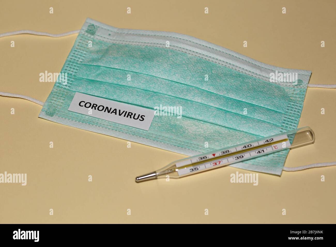 Maschera chirurgica protettiva con CORONAVIRUS di parola su di esso e termomemter primo piano isolato su sfondo color pastello. Foto Stock