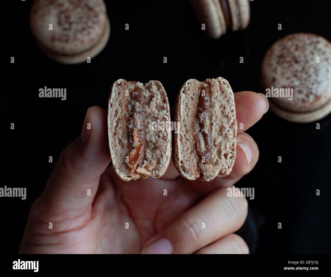 La mano contiene due metà di macaron di cioccolato Foto Stock