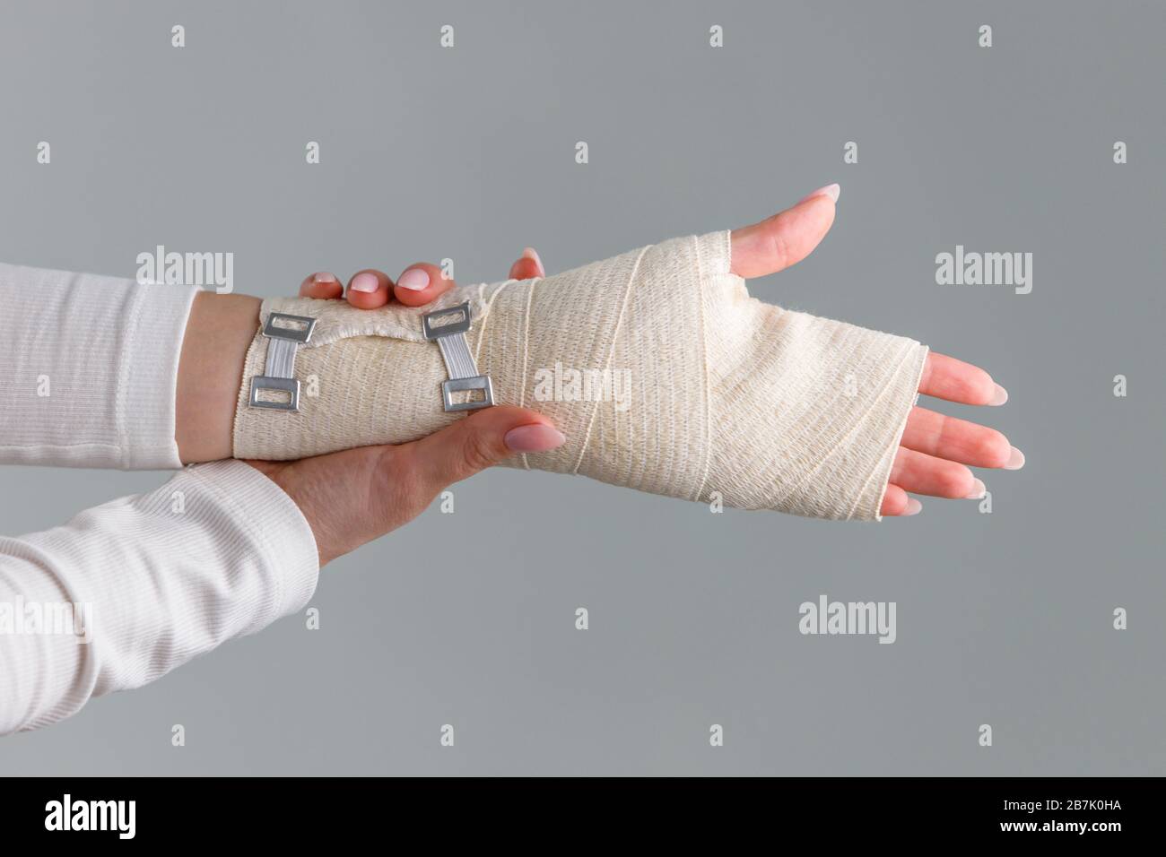 Primo piano delle braccia della donna che toccano il suo polso doloroso con bendaggio ortopedico elastico di supporto flessibile causato da un lavoro prolungato sul laptop. Tuna carpale Foto Stock