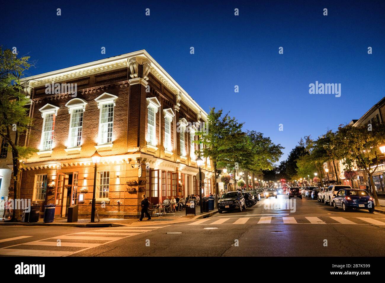 King Street Old Town Alexandria a Dusk Virginia // ALEXANDRIA, Virginia, Stati Uniti - il fondo di King Street nel centro storico di Alexandria al crepuscolo, dove la storica strada principale incontra il lungomare del fiume Potomac. La strada e' illuminata da calde luci stradali, che mostrano l'affascinante architettura coloniale e la movimentata attivita' di negozi e ristoranti mentre il giorno passa alla sera. Foto Stock