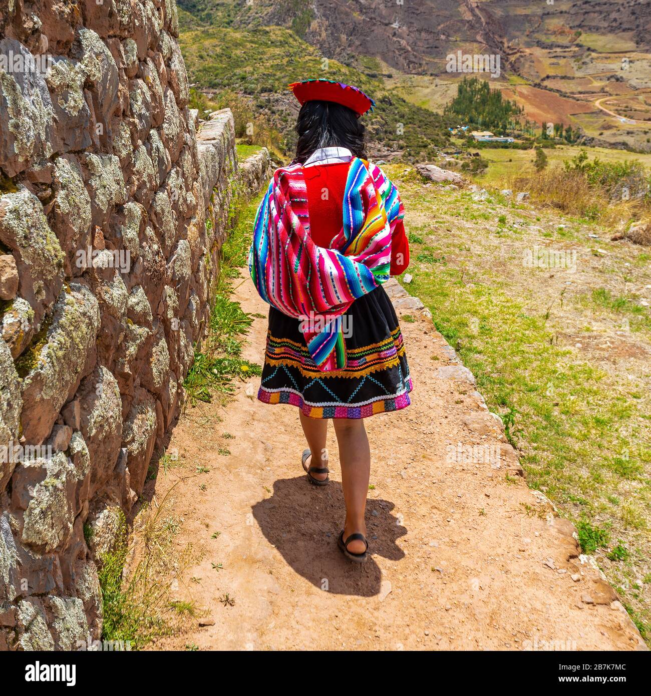Donna indigena Quechua con abbigliamento tradizionale che cammina lungo una strada inca e muro a Tipon, provincia di Cusco, Perù. Foto Stock