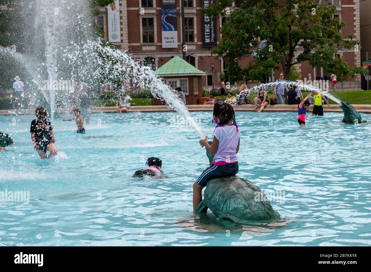 Giovane ragazza seduta sulla fontana di tartaruga che spara acqua dalla bocca, bambini che giocano e nuotano in una caratteristica ornata dell'acqua, a Philadelphia Foto Stock