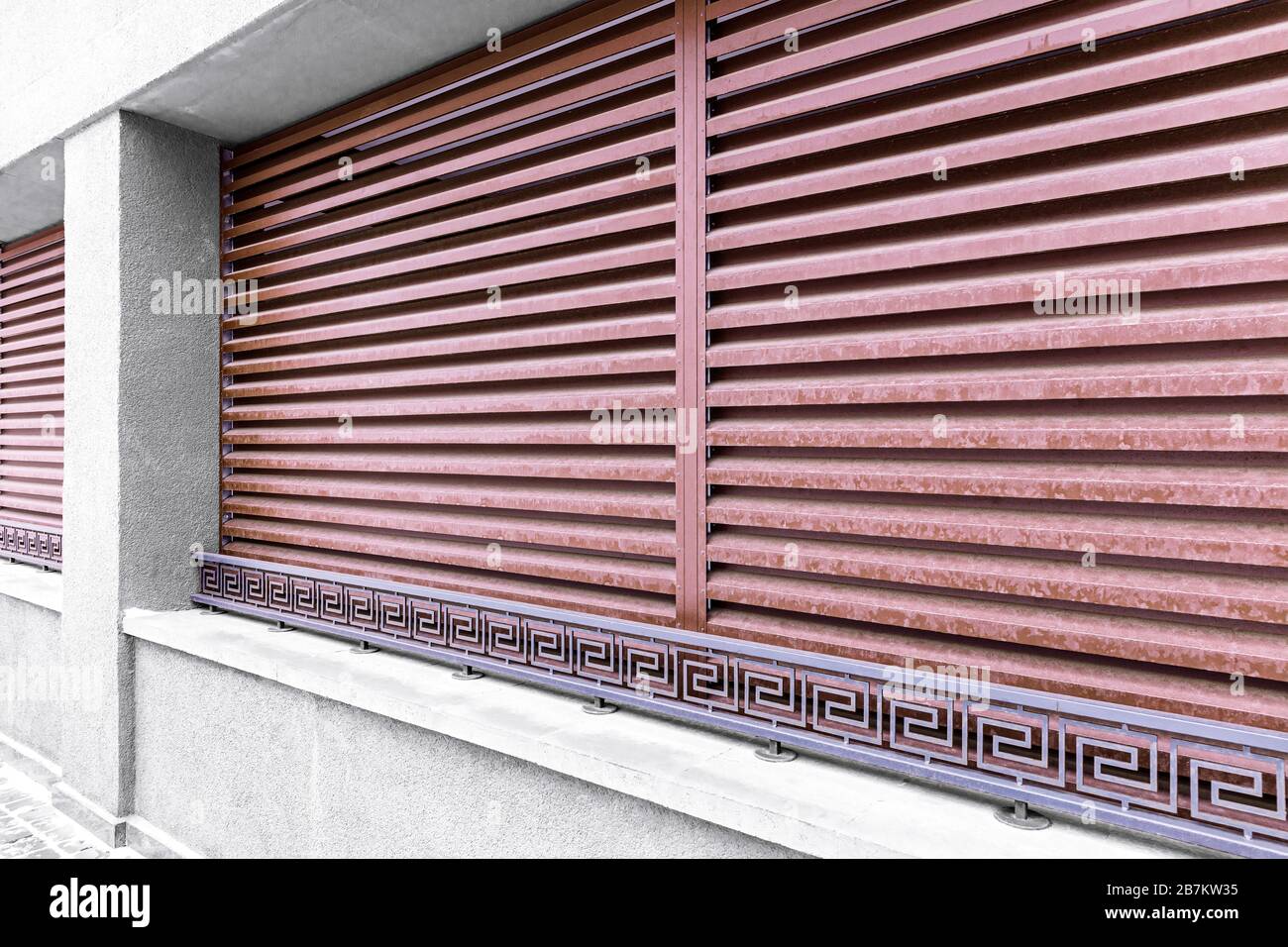 facciata di un edificio moderno con finestre a file, tende protettive in metallo rosso e ringhiere in metallo battuto Foto Stock