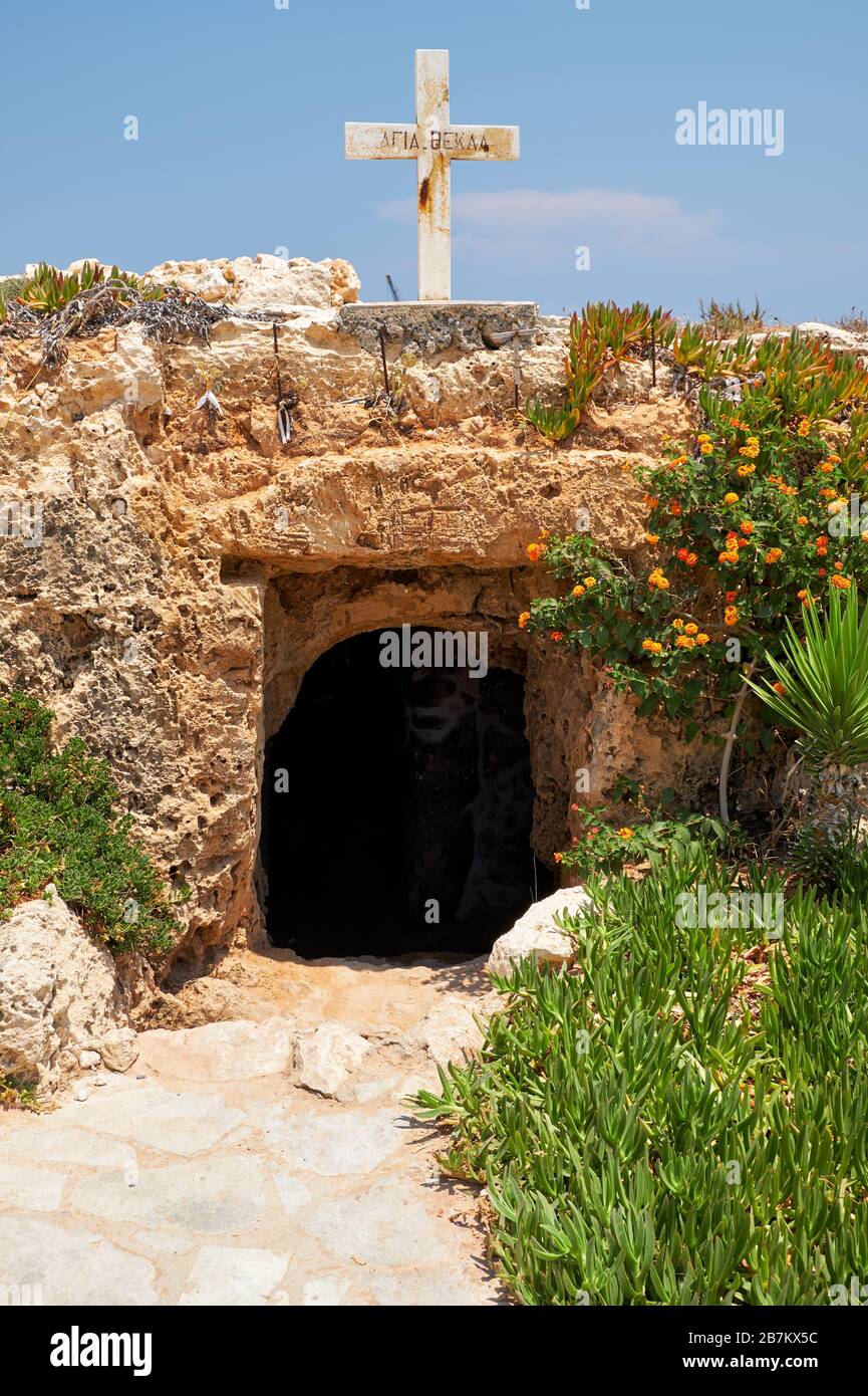 La piccola chiesa catacomba di Ayia Thekla (Agia Thekla), scolpita nella roccia del mare e la croce di pietra sulla sporgenza rocciosa sopra di essa. Ayia Napa. CYP Foto Stock