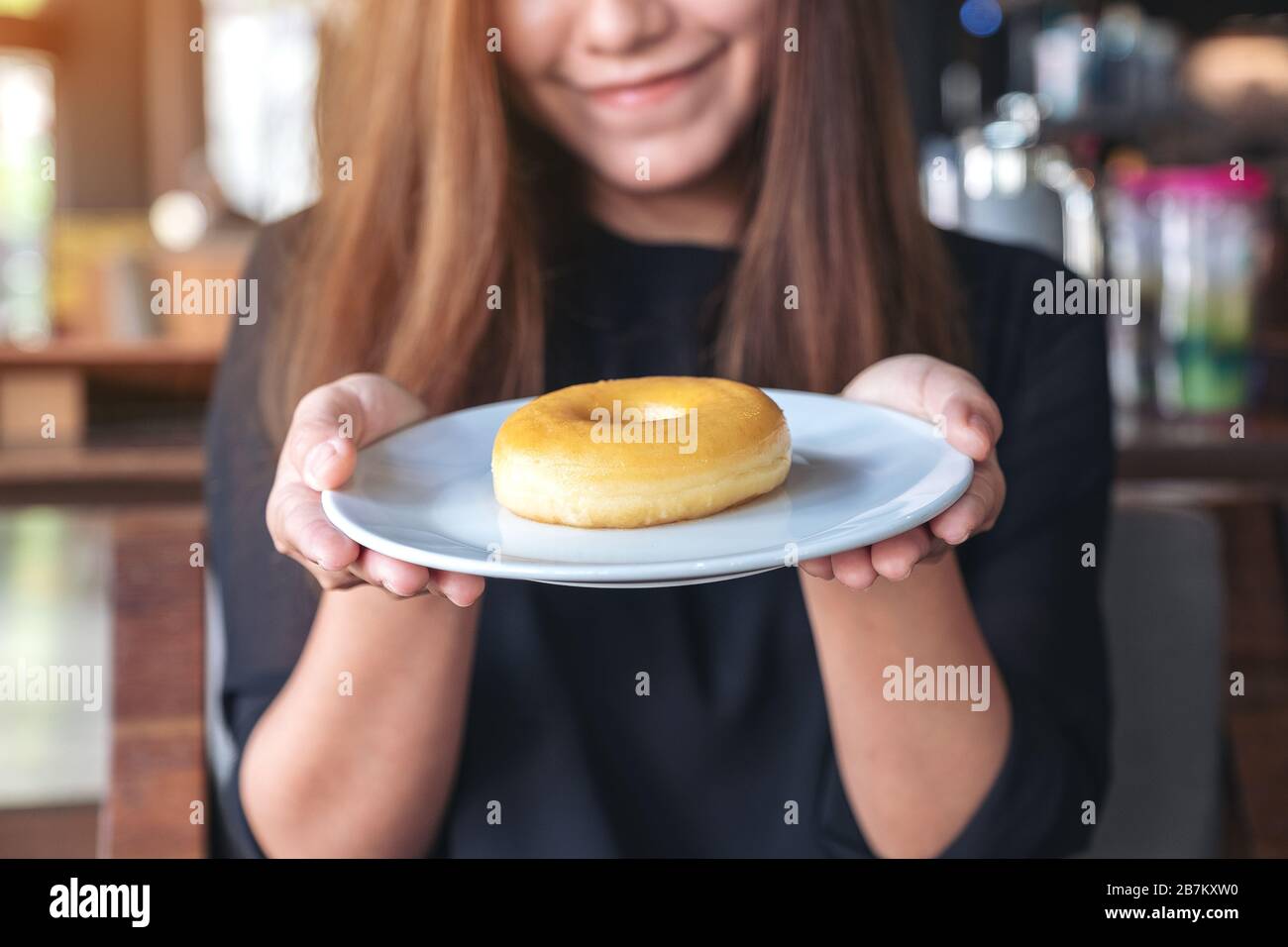 Una bella donna asiatica che tiene e mostra un piatto di ciambella con sentirsi felice e buon stile di vita nel moderno caffè Foto Stock