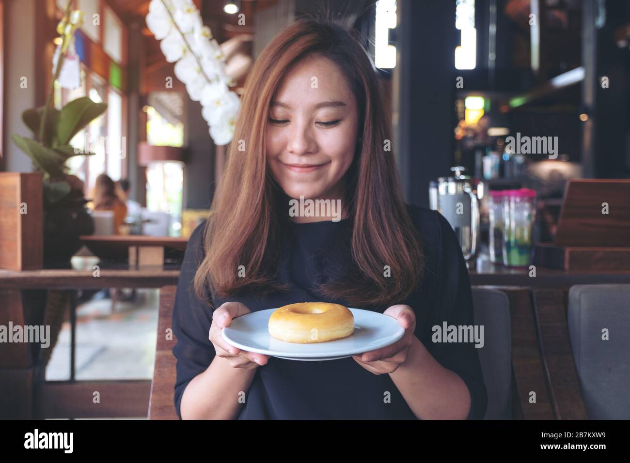 Una bella donna asiatica che tiene e mostra un piatto di ciambella con sentirsi felice e buon stile di vita nel moderno caffè Foto Stock