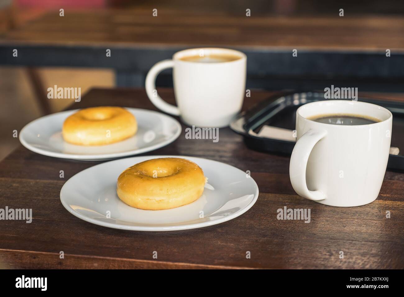 Due ciambelle in una piastra bianca con tazze da caffè su un tavolo di legno Foto Stock