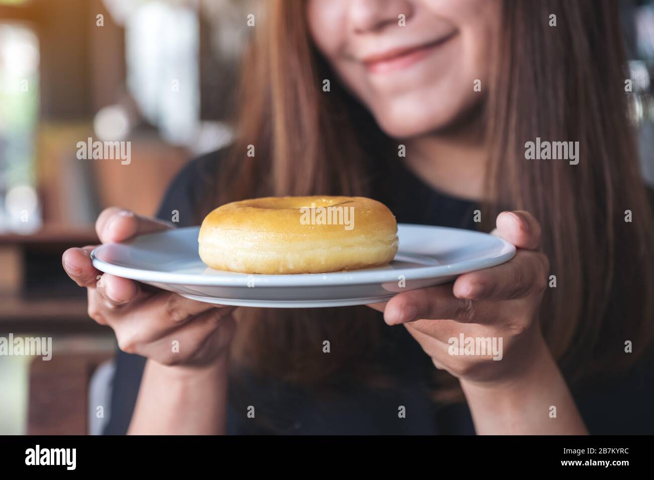 Una bella donna asiatica che tiene e mostra un piatto di ciambella con sentirsi felice e buon stile di vita nel moderno caffè Foto Stock