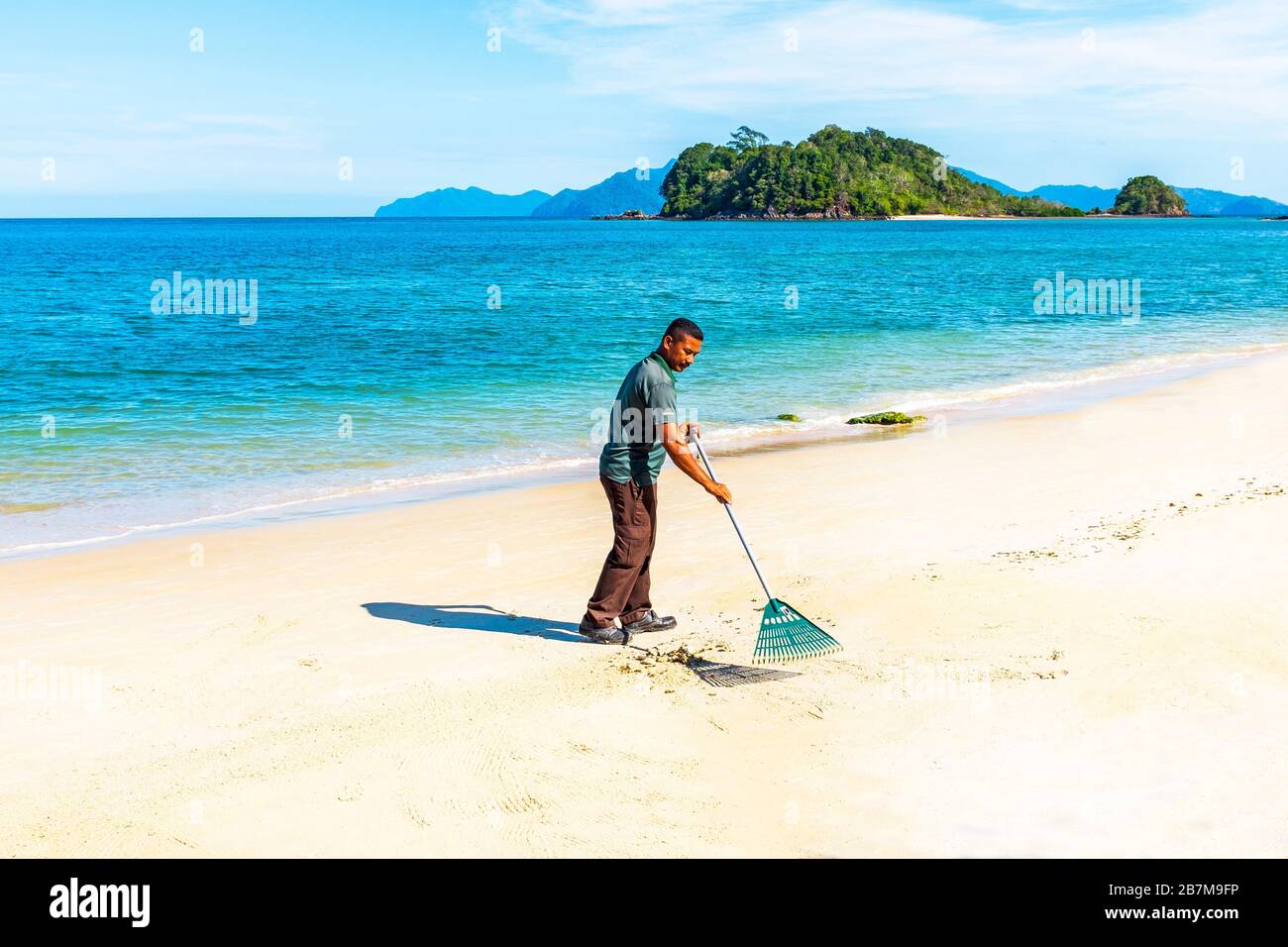 Uomo che rastrella e pulisce la spiaggia ad Andaman, Langkawi, Malesia, Asia Foto Stock