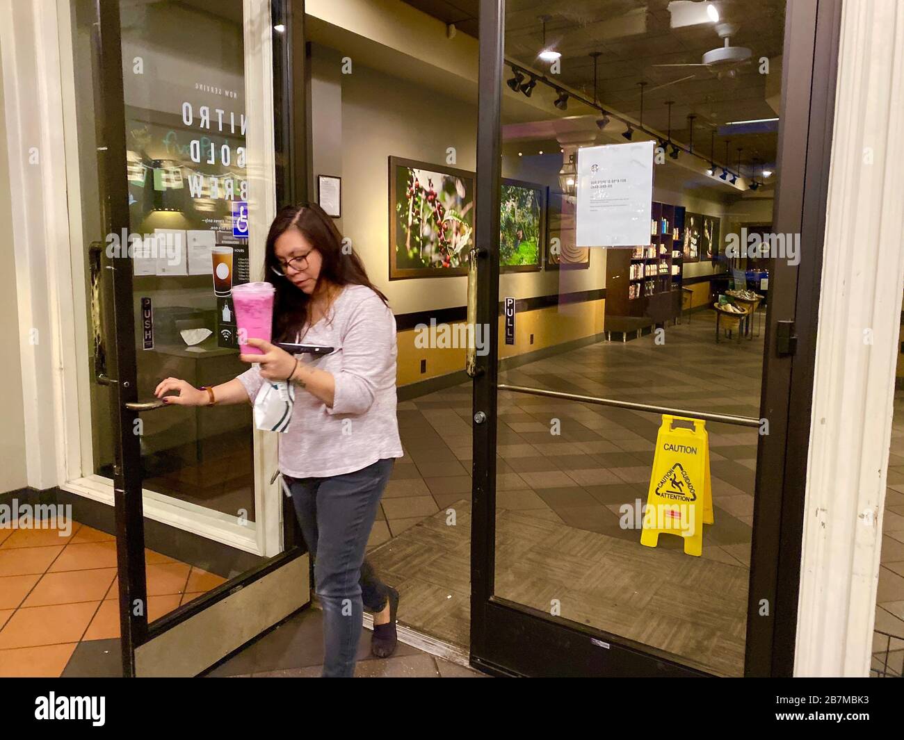 Santa Barbara, California, Stati Uniti. 16 Marzo 2020. Una donna porta la sua bevanda rosa da uno Starbucks vuoto, presso il Five Points Shopping Center di Santa Barbara, California, nel tardo lunedì pomeriggio durante la pandemia del virus Corona. Stanno servendo 'Grab and Go' ma hanno rimosso tutte le sedie e non consentono ai clienti di sedersi di lato o all'esterno. Credit: Amy Katz/ZUMA Wire/Alamy Live News Foto Stock