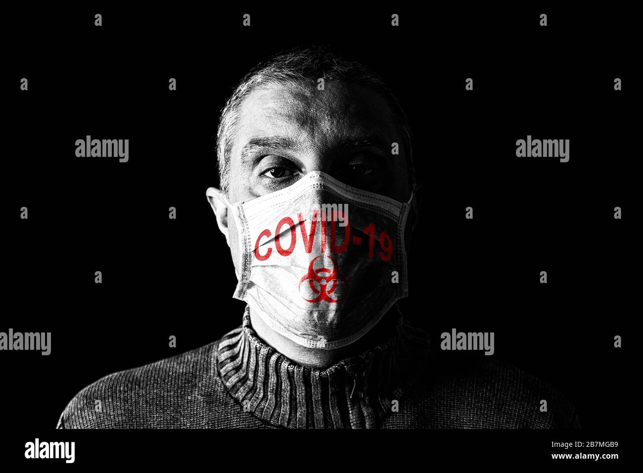 Uomo con maschera chirurgica. Biohazard e COVID-19, noto anche come simbolo di coronavirus. Pandemico o epidemico e spaventoso, paura o concetto di pericolo. Sfondo nero Foto Stock