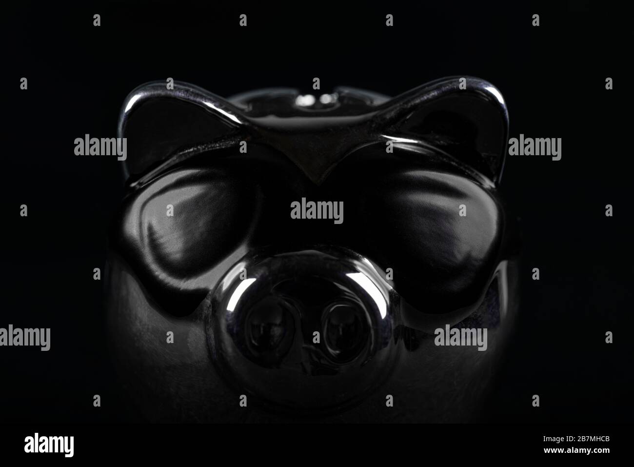 Una banca scura del piggy con le zone dell'occhio sta davanti ad un muro nero. Foto Stock
