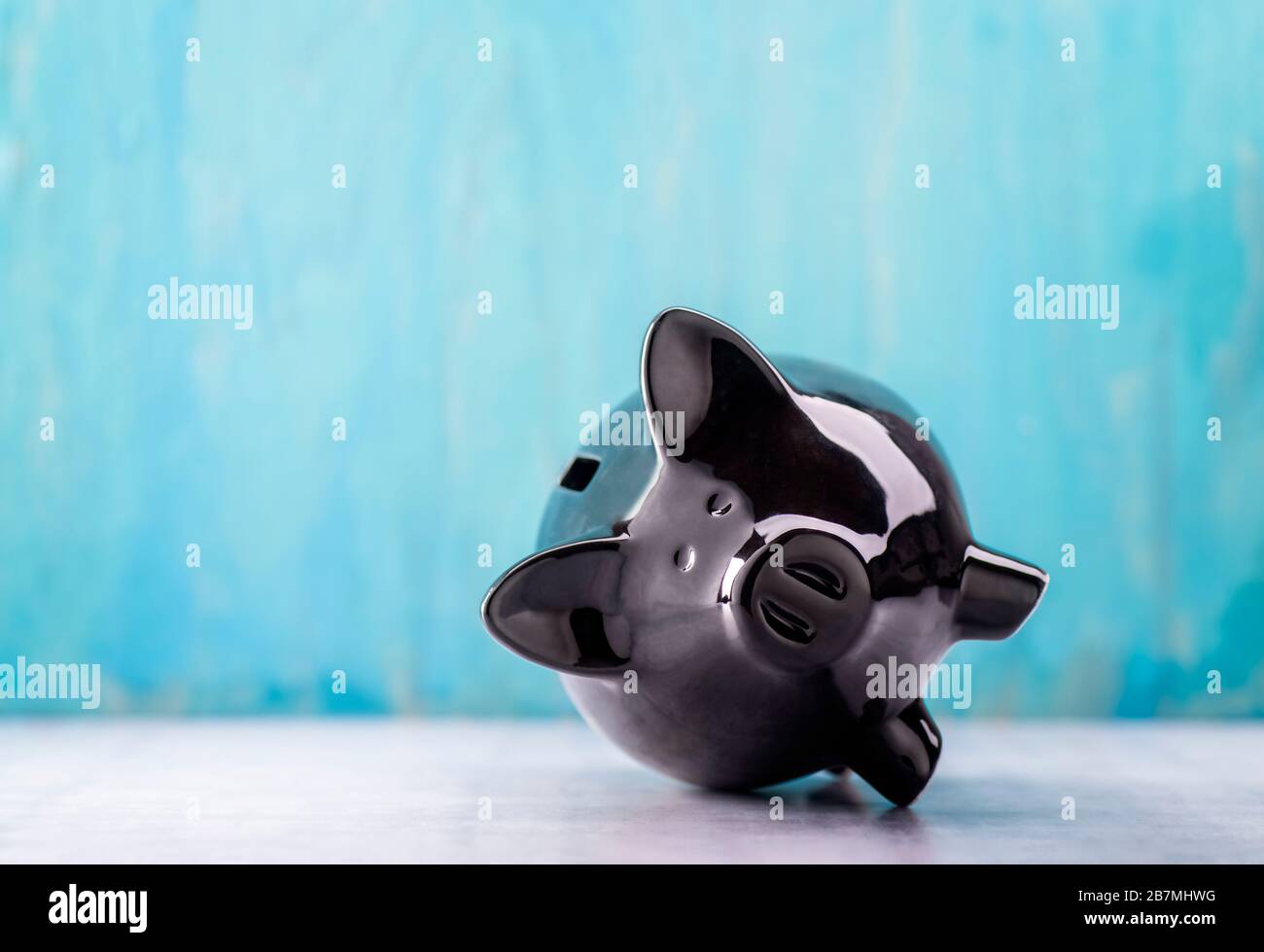 Una banca nera del piggy si trova contro un fondo turchese sul relativo lato Foto Stock