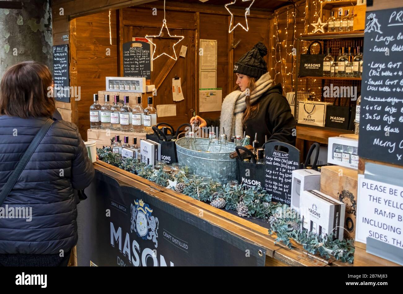 Giovane donna che vende bottiglie di Masons gin a St Nicholas Christmas Market Fayre York North Yorkshire Inghilterra Regno Unito GB Gran Bretagna Foto Stock