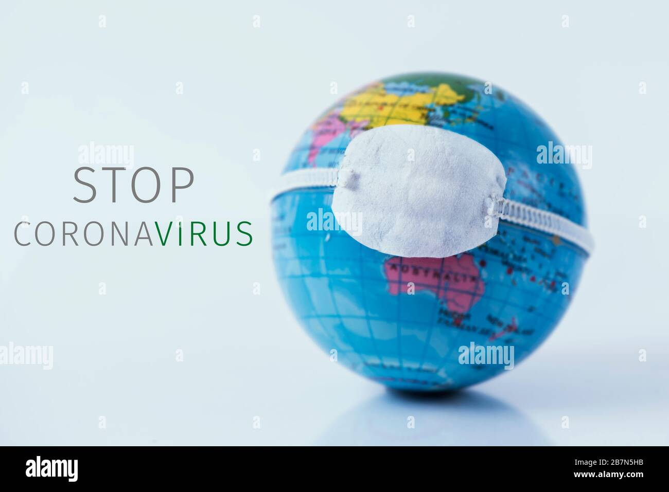 primo piano di un globo terrestre con una maschera protettiva e il testo fermare il coronavirus su uno sfondo bianco Foto Stock