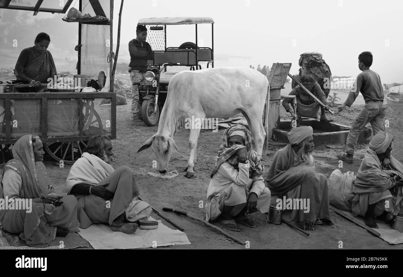 Gruppo di persone indù, alcuni mendicanti in cerca di elemosina, donna che vende tè, vacca Santa, e altri vicino al fiume Yamuna a Vrindavan, India. Foto Stock