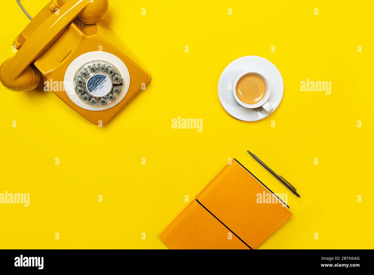 Disposizione gialla con telefono retrò rotante, tazza di caffè, penna e notebook. Disposizione piatta, vista dall'alto, spazio copia. Foto Stock