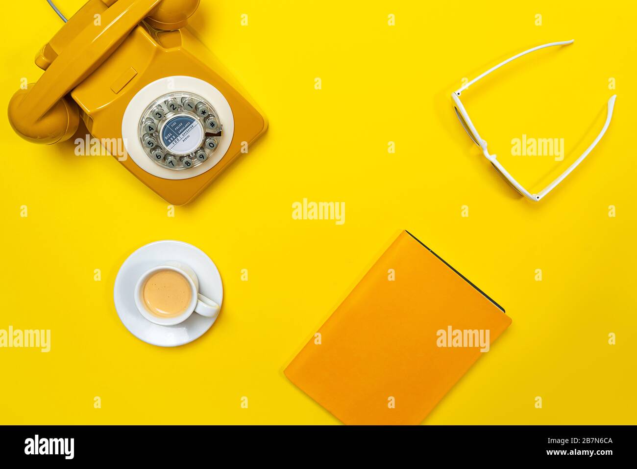 Disposizione gialla con telefono retrò rotante, tazza di caffè, occhiali da sole e notebook. Disposizione piatta, vista dall'alto, spazio copia. Foto Stock