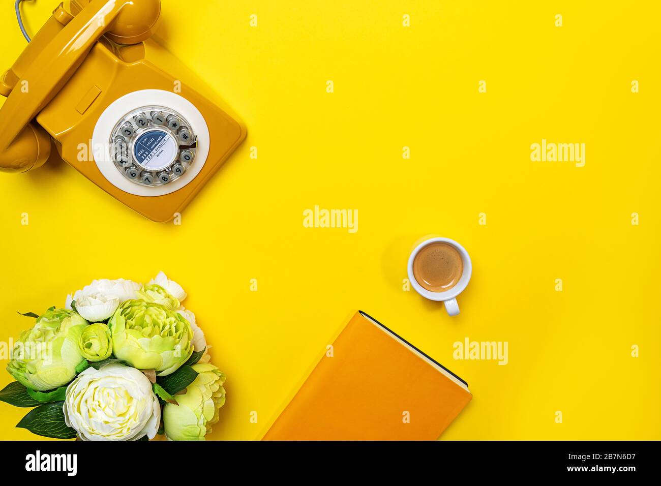 Disposizione gialla con telefono retrò rotante, tazza di caffè, fiori e notebook. Disposizione piatta, vista dall'alto, spazio copia. Foto Stock