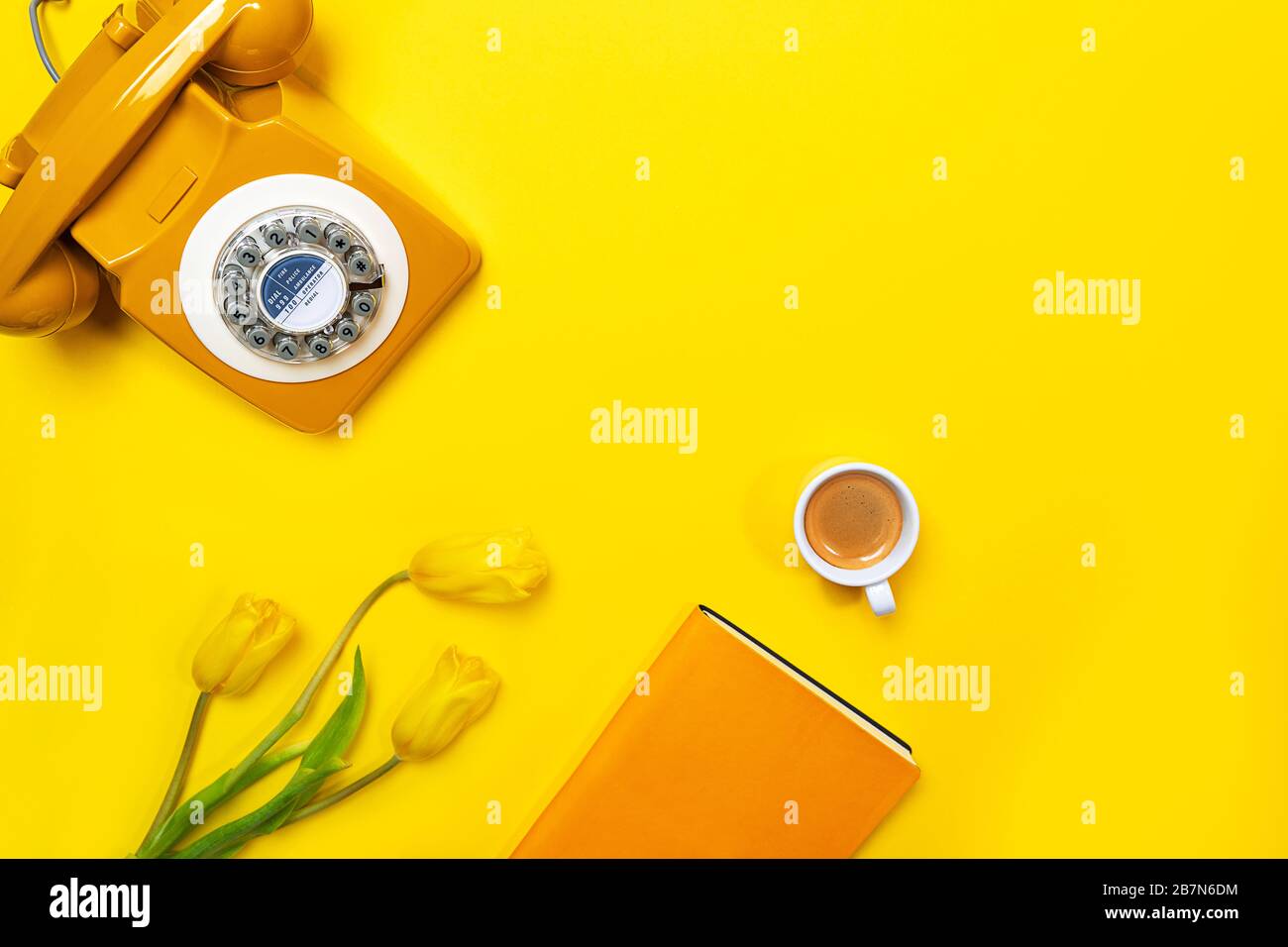 Disposizione gialla con telefono retrò rotante, tazza di caffè, fiori e notebook. Disposizione piatta, vista dall'alto, spazio copia. Foto Stock