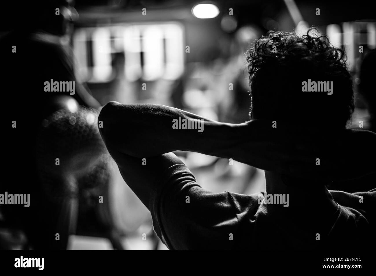 Un primo piano selettivo fuoco atmosferico scatto in bianco e nero. Un uomo muscoloso si rilassa al chiuso, con le mani dietro la testa. Silhouette maschile da dietro. Foto Stock