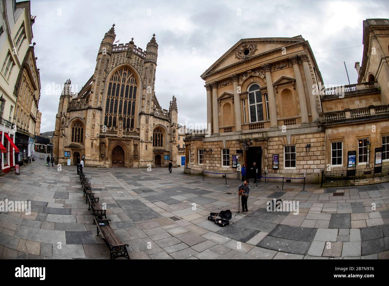 Un busker gioca in una piazza vuota di fronte all'abbazia di Bath e alle terme romane dopo che il governo ha annunciato misure più severe per combattere Coronavirus. Foto Stock