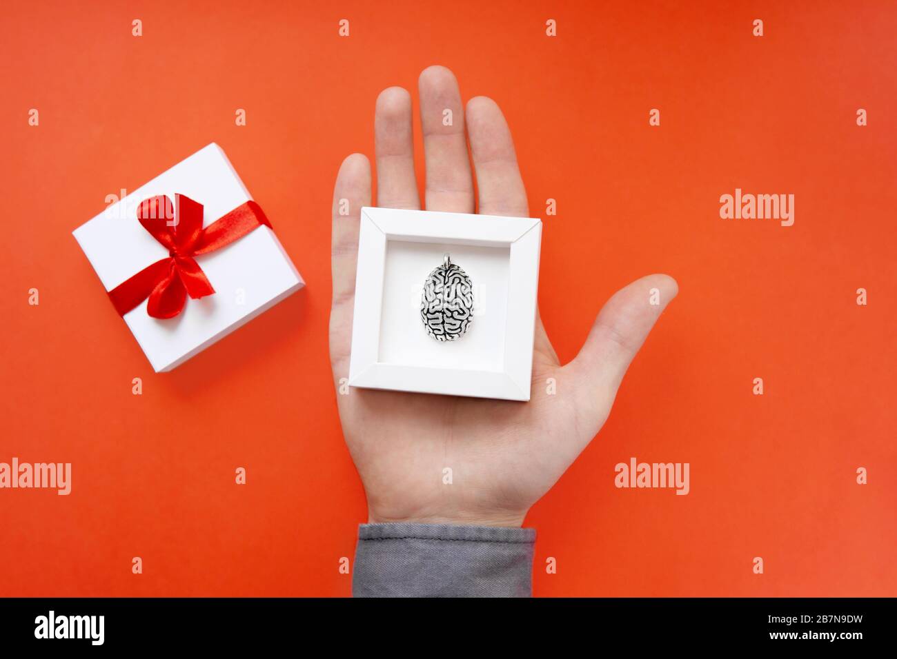 Palmo maschio che contiene una scatola regalo bianca con un modello in acciaio di un cervello umano all'interno. Un concetto saggio di regalo. Foto Stock