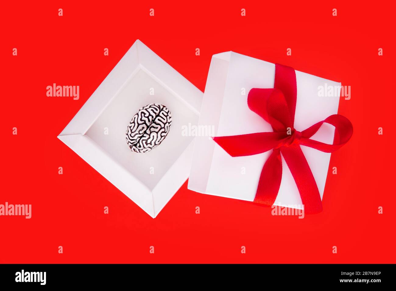 Regalo creativo a un genio in forma di una piccola copia metallica di un cervello umano all'interno di una scatola regalo bianca con un nastro rosso e arco sulla copertina. Foto Stock