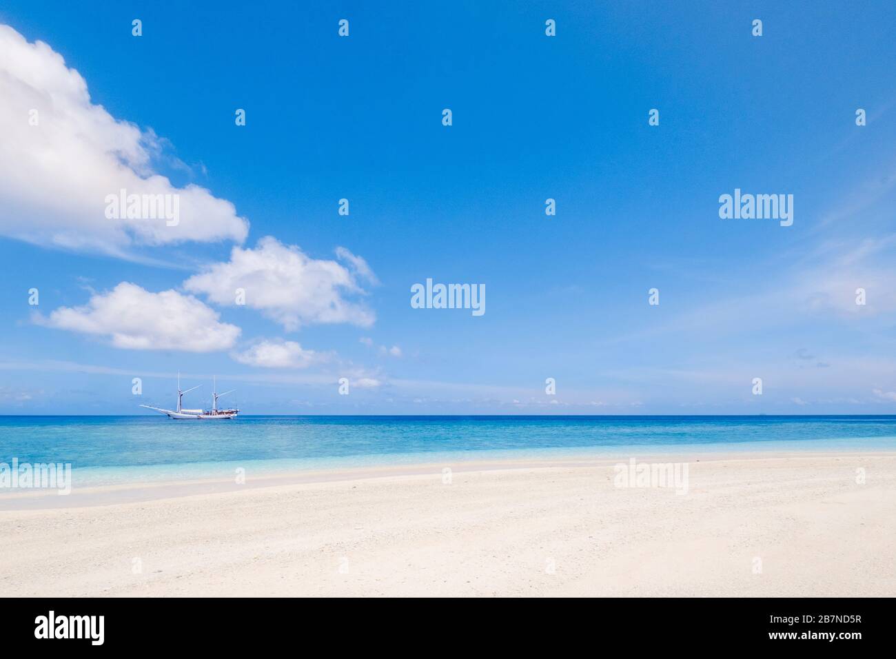 Un'alta nave ormeggiata su un oceano tropicale di fronte ad una spiaggia incontaminata Foto Stock