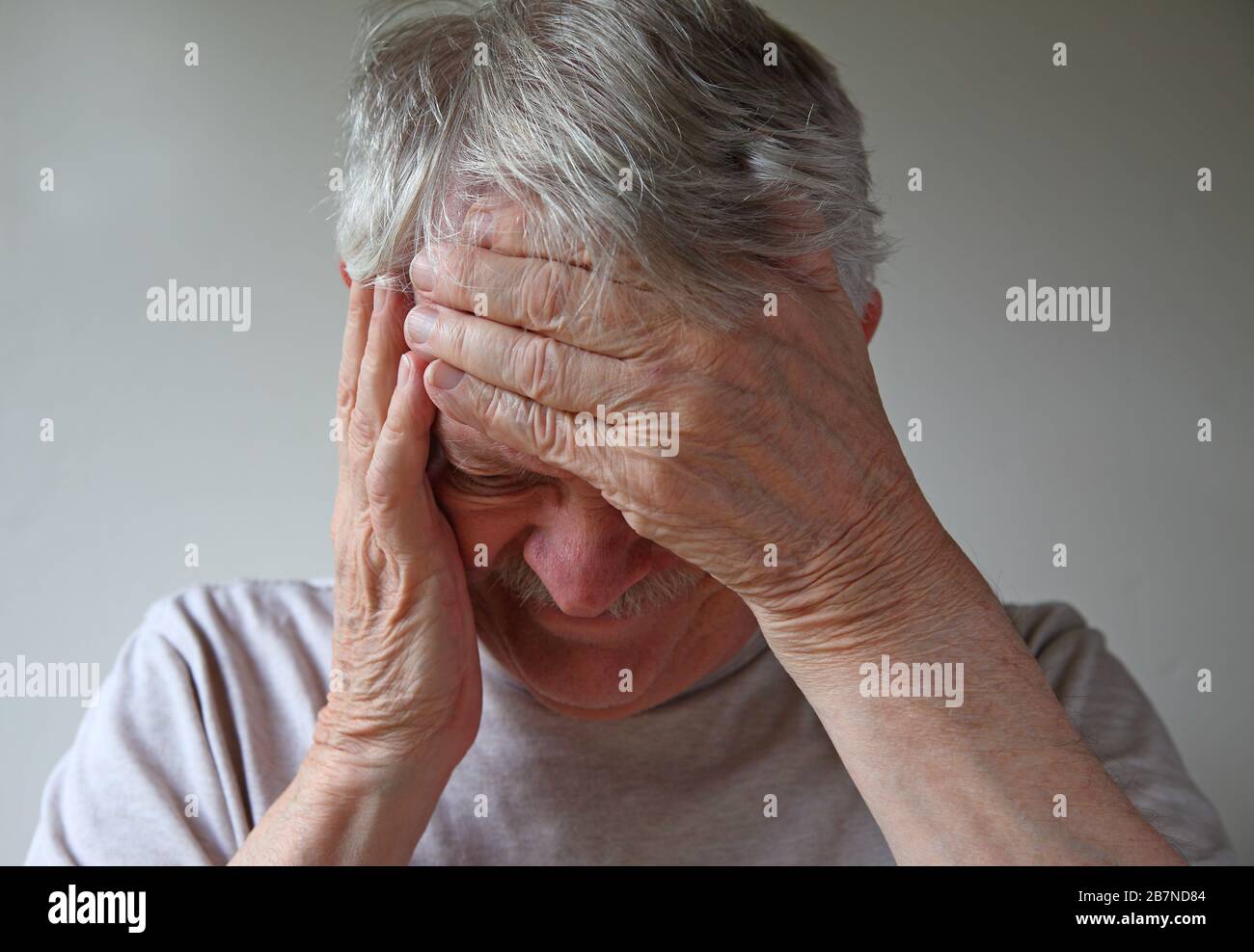 Uomo più anziano con le mani sulla fronte e sul lato del viso Foto Stock