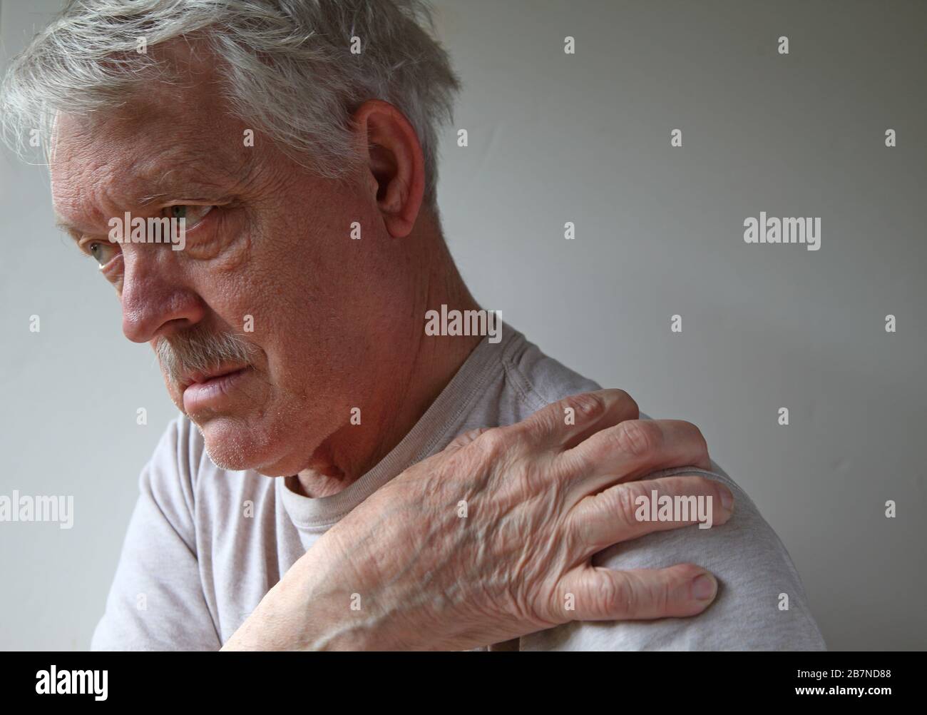 Uomo anziano con una spalla dolorosa in luce naturale Foto Stock