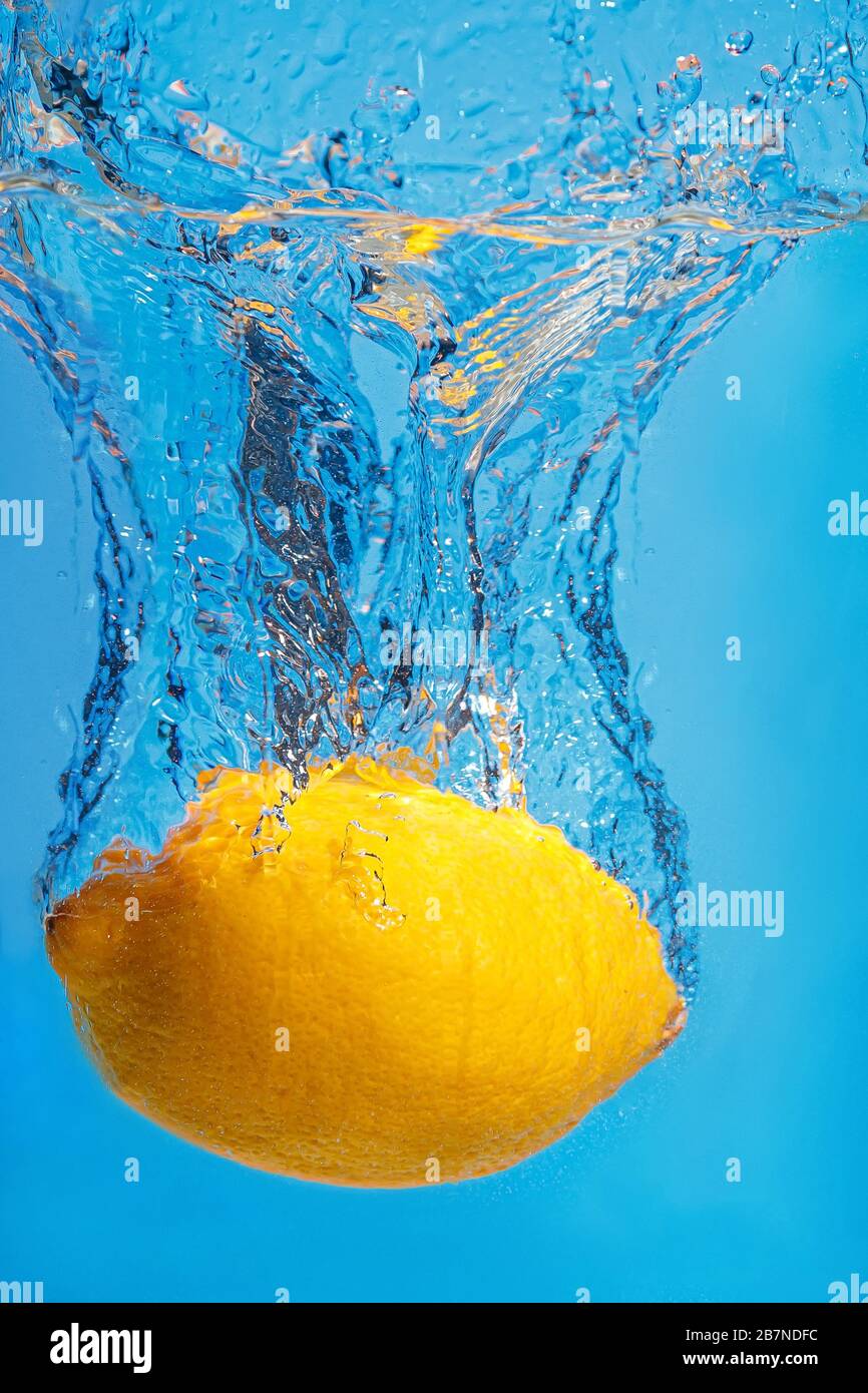 Gocce di limone fresco in acqua con uno spruzzo su sfondo blu Foto Stock