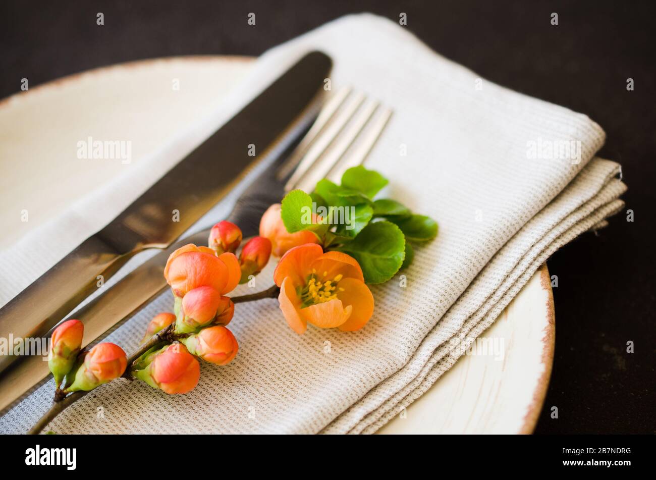 Vintage impostazione tabella con delicati fiori su un tovagliolo di lino su uno sfondo scuro, close-up. Tabella di festa insieme con decorazioni floreali Foto Stock